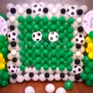 The wall is decorated with bunches of green, white and yellow balloons.