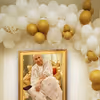 The balloon arch of CherishX's Guruji Birthday Decor is made with white. golden chrome and Golden Confetti balloons.