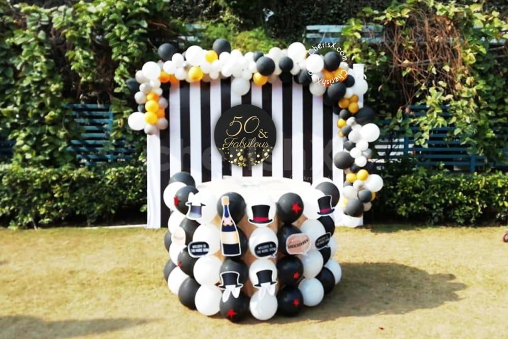 The Black and Golden Decor includes this table decorated with White Latex and Black Latex balloons placed with Black and white strips backdrop.