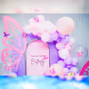 The decor features graceful butterfly cutouts and a delightful blend of purple and pink balloons.