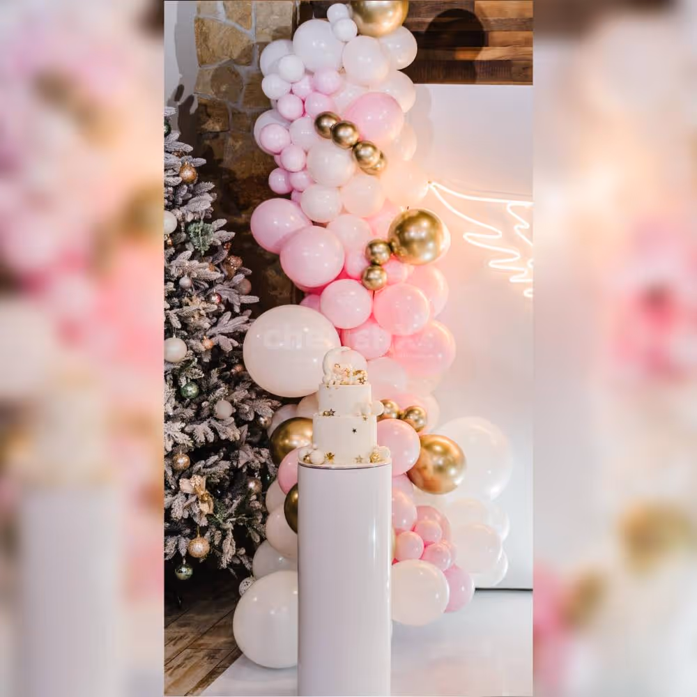 Experience the magic of the heartwarming baby shower decor with a backdrop of pink flex, adorned with a winged neon light and an arch of balloons in white, pastel pink, blush pink, and chrome, creating a whimsical and charming ambiance.