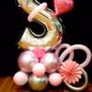 The balloon bouquet is complemented by pretty pink rosettes, pink grass, and an assortment of pink and silver chrome BT balloons.
