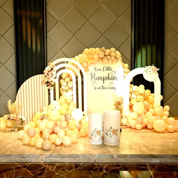 A charming pumpkin-themed baby shower consists of sunboard cutouts with stands, draped in 500 pastel balloons of peach, apricot, and chocolate brown.