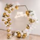 Elegant white and gold anniversary decoration by CherishX with balloon ring backdrop, flowers, and neon sign.
