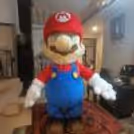 A life-sized Mario character with the iconic red hat and blue overalls, ready to entertain children at a birthday party.