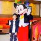 Standing next to the birthday cake, a Mickey Mouse live character at the celebration.