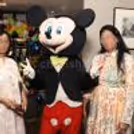 Child having a picture taken with the Mickey Mouse mascot at an indoor party.
