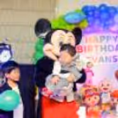 Mickey Mouse mascot with a child in front of a Happy Birthday display.