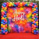 A stunning, lifelike “Happy Holi" banner is a colorful backdrop for a picture