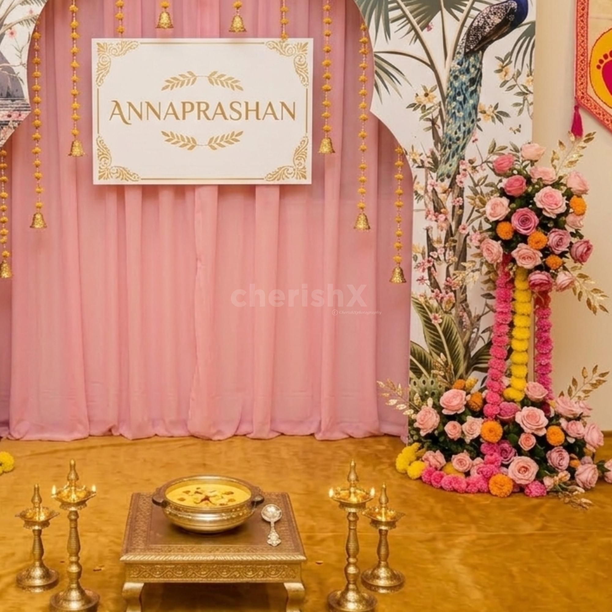 Customized Annaprashan Board With Festive Decoration And Pink Crepe Fabric Draping At The Back.