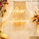 Happy Anniversary neon sign with warm white on a background of hanging tassels and lights.