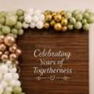 Elegant decoration of an anniversary setup with a vintage wooden panel, organic balloon arch and white balloons at the base.