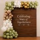 A backdrop with a green, white, gold and rose gold balloon garland, saying “Celebrating Years of Togetherness”.