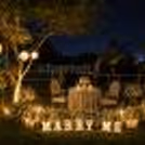candlelight proposal setup with white floral arrangements on a lush lawn, creating a timeless romantic ambiance.