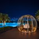 Private glass dome dining experience beside a beautifully lit swimming pool.