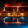 Luxury poolside dining setup with glowing candles, dramatic landscape lighting, and reflections on tranquil blue water.