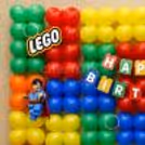 Lego Style Superhero Character Attached To A Multicoloured Balloon Display With Block-Inspired Decoration.