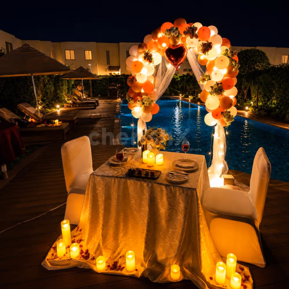 Romantic poolside dinner setup with balloon arch, candlelight, and luxury outdoor dining décor.