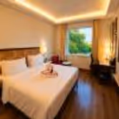 Elegant hotel room featuring a king bed, contemporary décor, cozy seating area, and large window overlooking lush greenery.