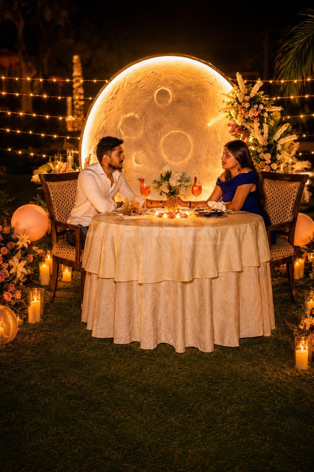 Couple enjoying a private moonlit candlelight dinner with floral décor, glowing candles, and a giant illuminated moon backdrop at Umrao.