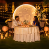 Luxe Moonlit Candlelight Dinner by Umrao showcasing a romantic private dining setup with candles, flowers, fairy lights, and a glowing moon backdrop.