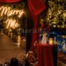 Proposal Table With Some Red Draping, A Vase Of Faux Roses, And Ambient Lighting On The Floor.