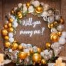 Romantic proposal with chrome gold, white balloons and greenery backdrop.
