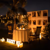 Romantic candlelight dining setup with a personalized photo wall, floral décor, and glowing candles for couples.