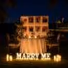 Proposal setup with flower arrangements, candles and backdrop photo for a proposal dinner outdoors.