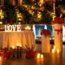 Elegant candlelit poolside dining arrangement featuring red roses, glowing LOVE letters, warm candles, and a beautifully lit blue pool backdrop