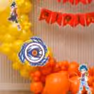 Yellow and orange balloon decoration with a Beyblade spinning top on a ring stand background.