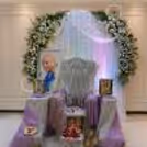 For Guru Ji Darshan, a white floral arch, drapes, a spiritual chair and a framed portrait.