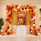 Orange, maroon, white and golden balloon garland around a framed spiritual portrait, Guru Ji birthday decoration.