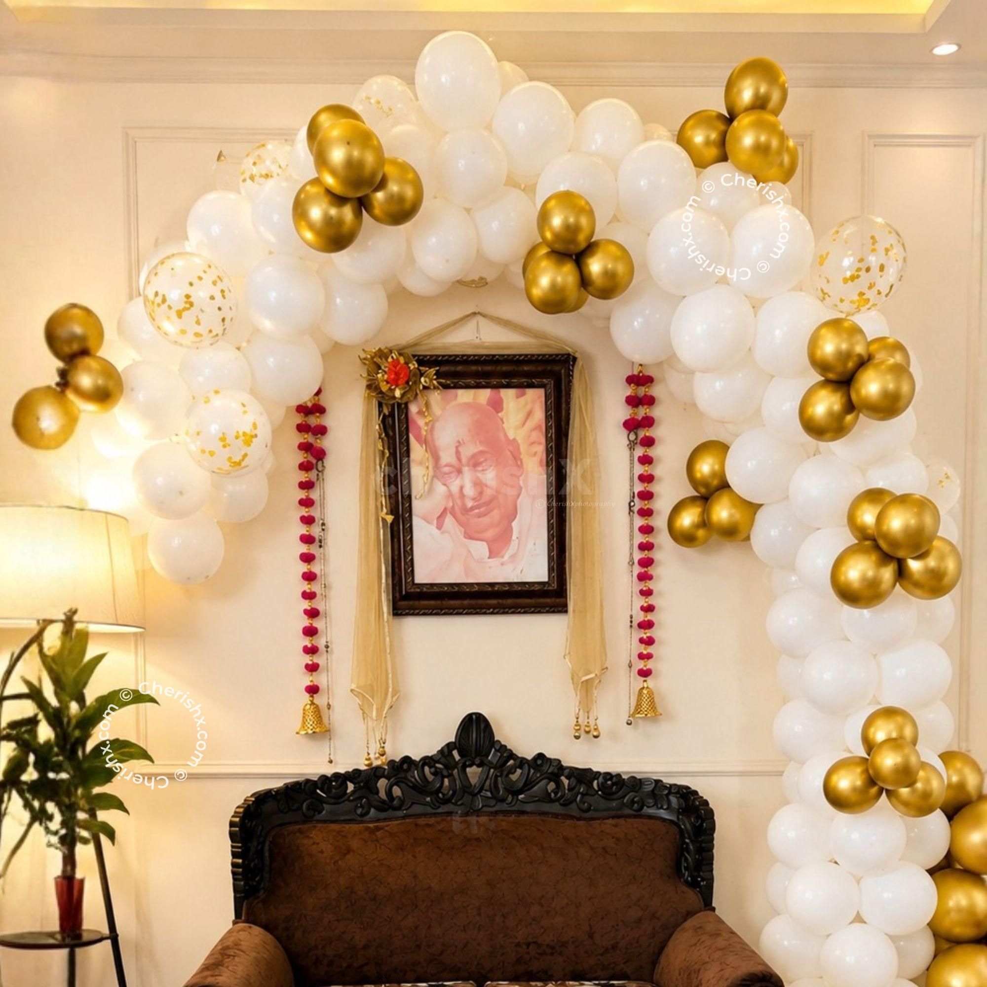 The balloon arch of CherishX's Guruji Birthday Decor is made with white. golden chrome and Golden Confetti balloons.