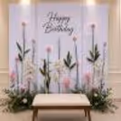 Elegant Sunboard Garden Birthday Backdrop With Pastel Artificial Flowers And Lush Green Leaf Design.