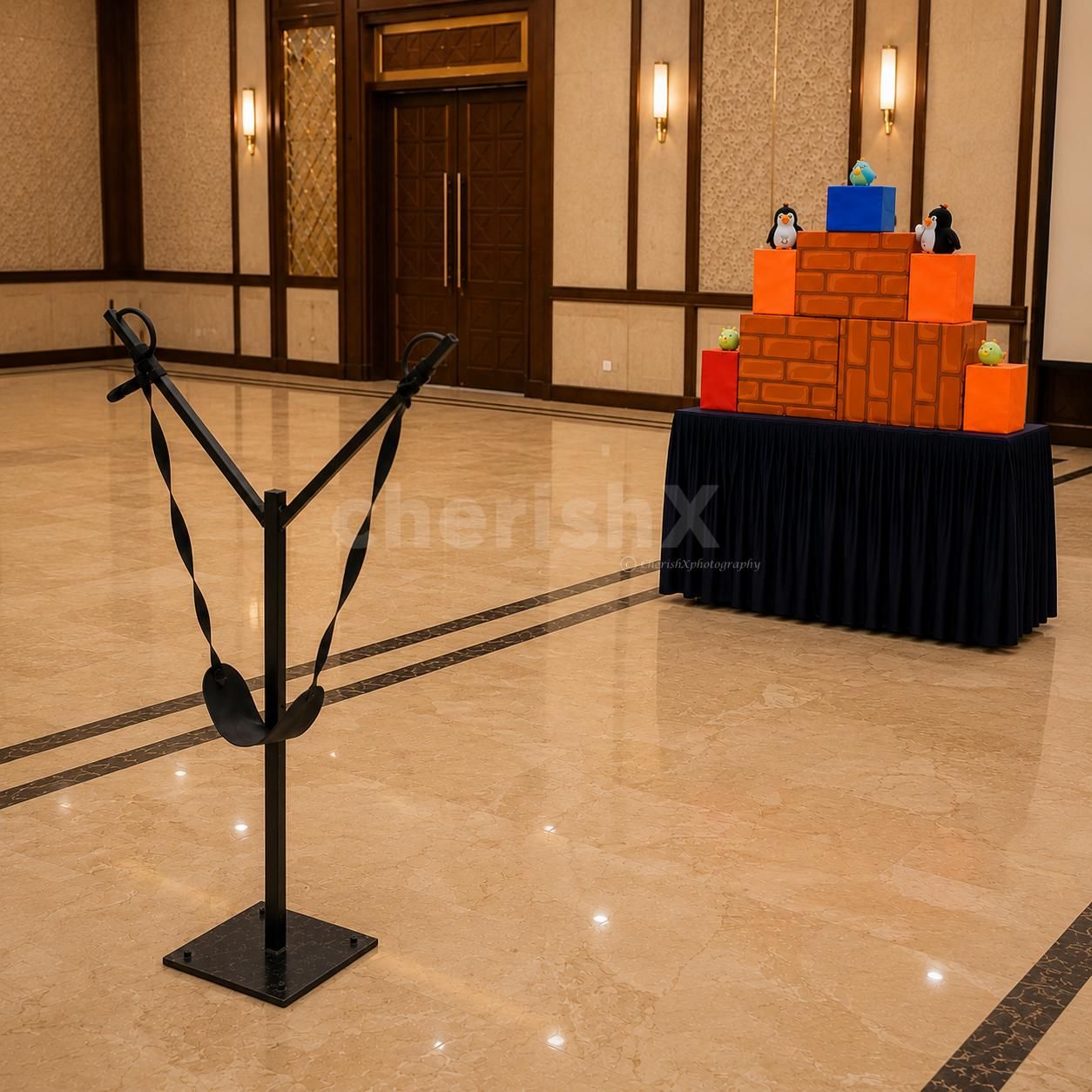 Indoor Angry Birds slingshot game setup in a banquet hall featuring a giant slingshot launcher and colorful block target for kids' parties.