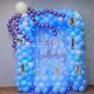Party Lighting And Pastel Balloon Clusters Frame A Blue Fringe Backdrop With A Curved Shape.