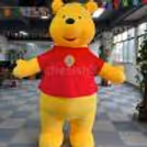 Front view of the soft cartoon costume with a monkey performer in the background
Full-length costume, one hand raised, showing bright colours and friendly cartoon design.
