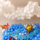 Happy birthday balloon wall with fluffy white cloud balloons, bunting, golden star foil balloon, and airplane theme.