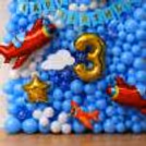 Close up of birthday balloons backdrop with airplane theme, golden digit foil balloon and blue balloon wall with paper cutouts.