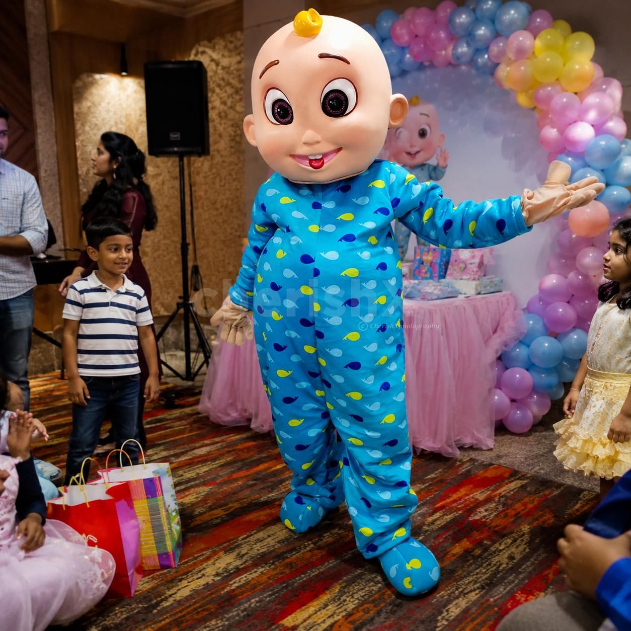 Cocomelon mascot with children holding photos at an outdoor holiday party.