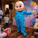 Cocomelon mascot with children holding photos at an outdoor holiday party.
