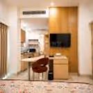Modern hotel suite with a kitchenette, dining table, smart TV, and contemporary wooden interiors.