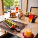 Romantic table setup with sushi, mocktails, candles, and gourmet dishes beside a large window overlooking lush greenery.