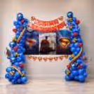 A full-size Superman birthday backdrop with blue balloon pillars, superhero flex panels, bubble balloons and a red Happy Birthday banner.