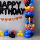 Side view of cut-outs with characters, layered balloon columns, decorative curls and themed party information for a kids party.