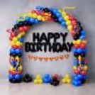 Superhero party background with colourful arch, black foil birthday letters, comic accents and matching clusters of floor balloons.