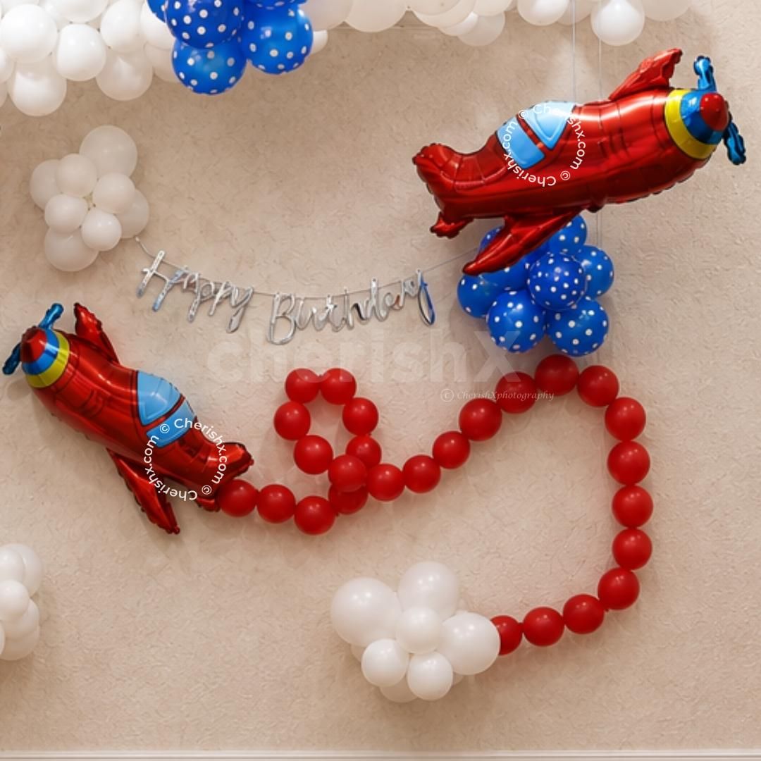 The lower decoration features a red balloon path, silver cursive birthday bunting, soft white balloon bunches and a balloon airplane foil plane.