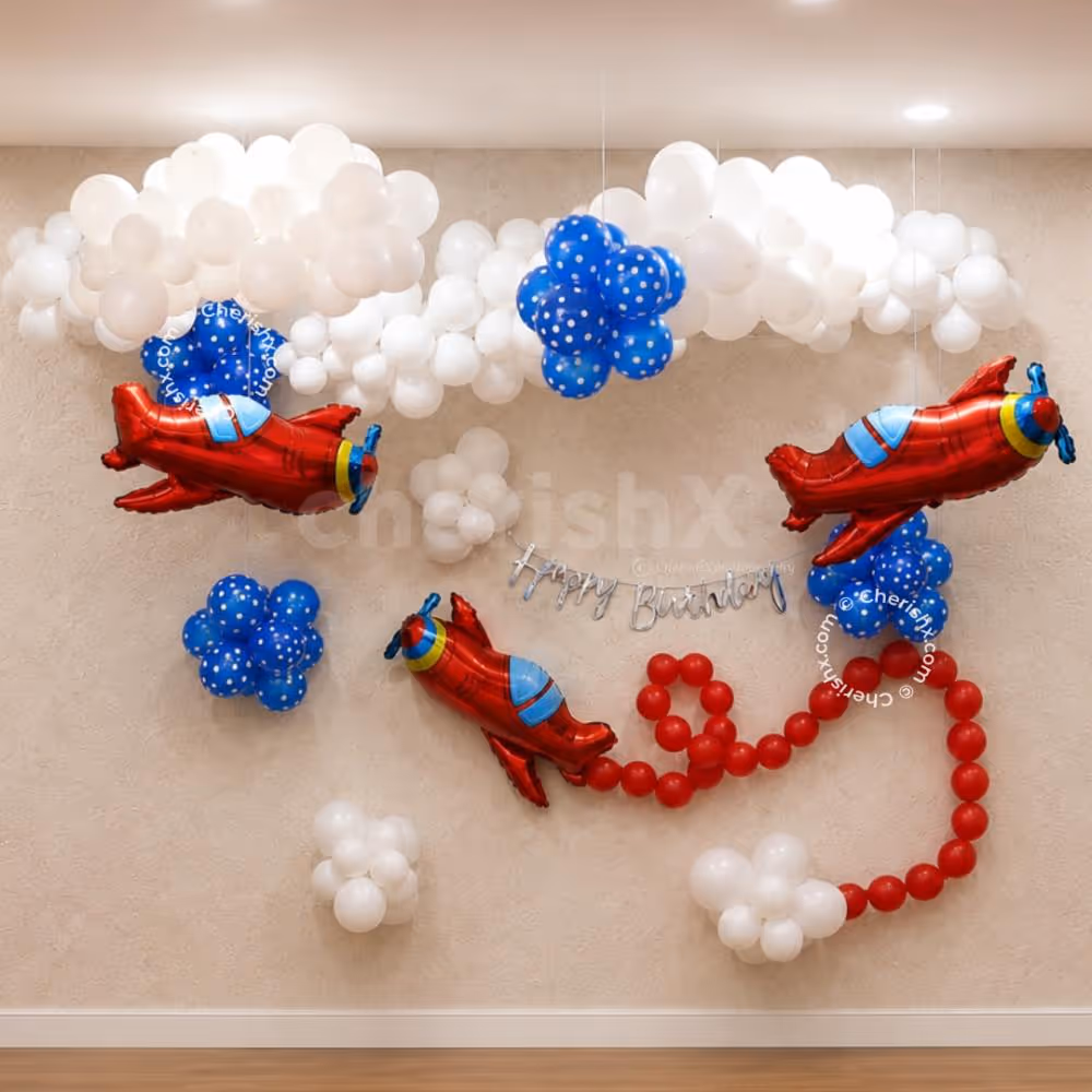 Fully decorated airplane birthday with floating white balloon clouds, 3 red airplane foil balloons, blue balloon clusters, and a silver Happy Birthday banner.