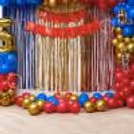 Wonder Woman birthday backdrop with columns of balloons, themed paper cutouts, metallic curtains in the background and balloons decorating the floor.